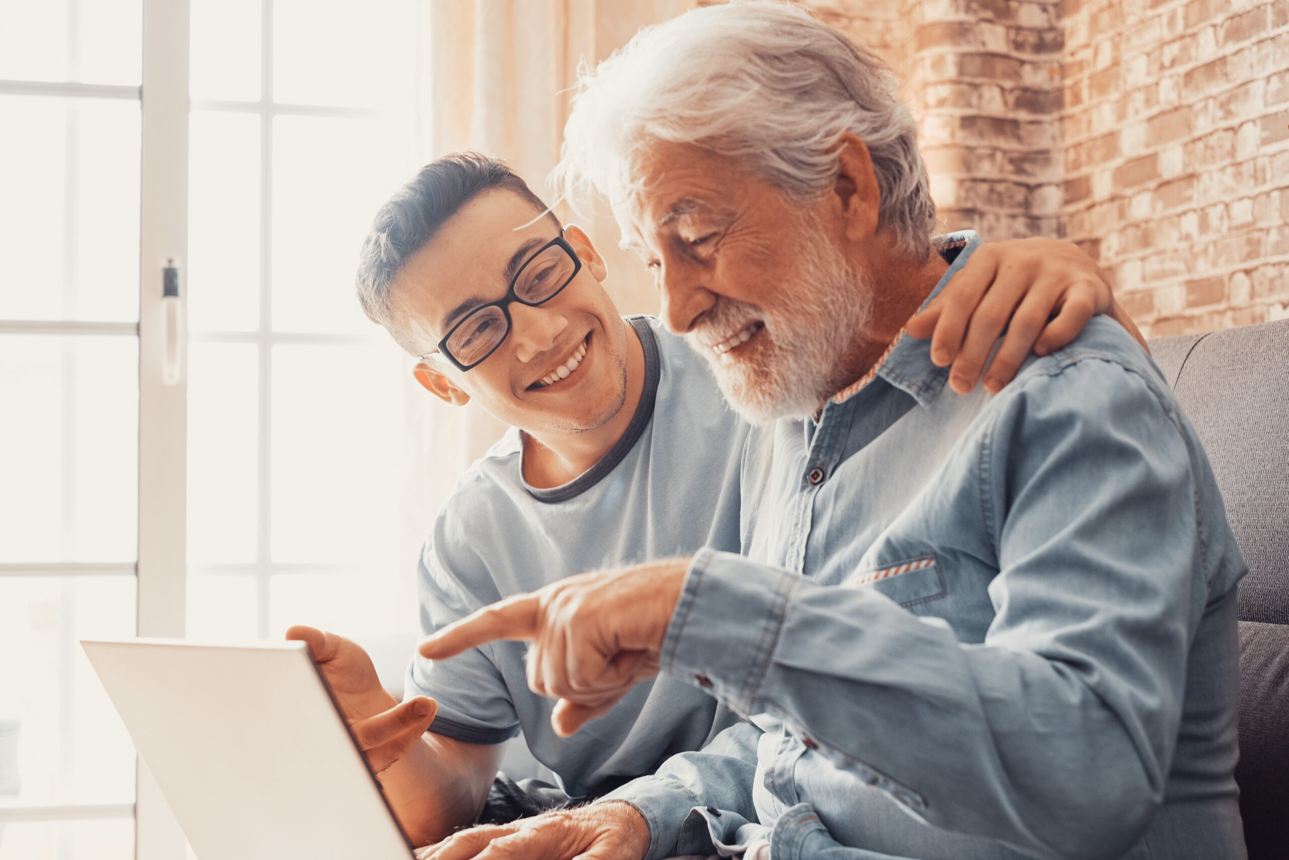 Smiling young boy helping senior grandfather with laptop choose goods or services via internet or web surfing together at home. Younger generation caring about older relatives teaching using computer